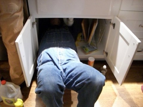 Plumber repairing under-sink plumbing in a kitchen cabinet